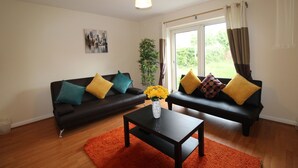 A living room with two black sofas, orange rug, and a vase with yellow flowers on a coffee table. - Depedale House (Derby)