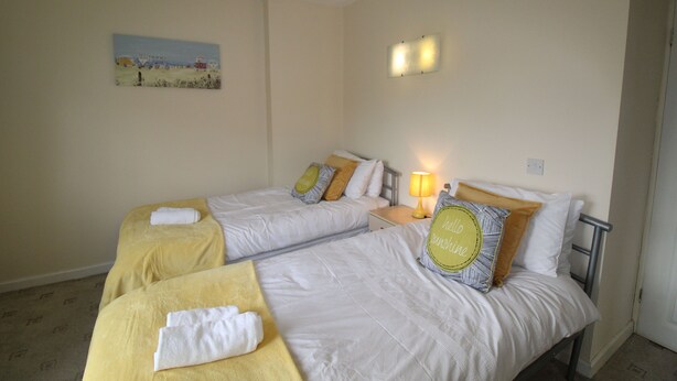 A hotel room with two beds, each with a yellow towel and a pillow. There is a painting on the wall and a lamp on the nightstand. - Depedale House (Derby)