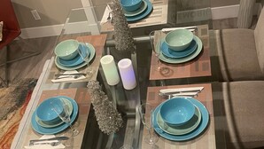 Zona pranzo con tavolo in vetro apparecchiato per quattro persone, con piatti blu e posate, circondata da sedie rivestite in grigio.
