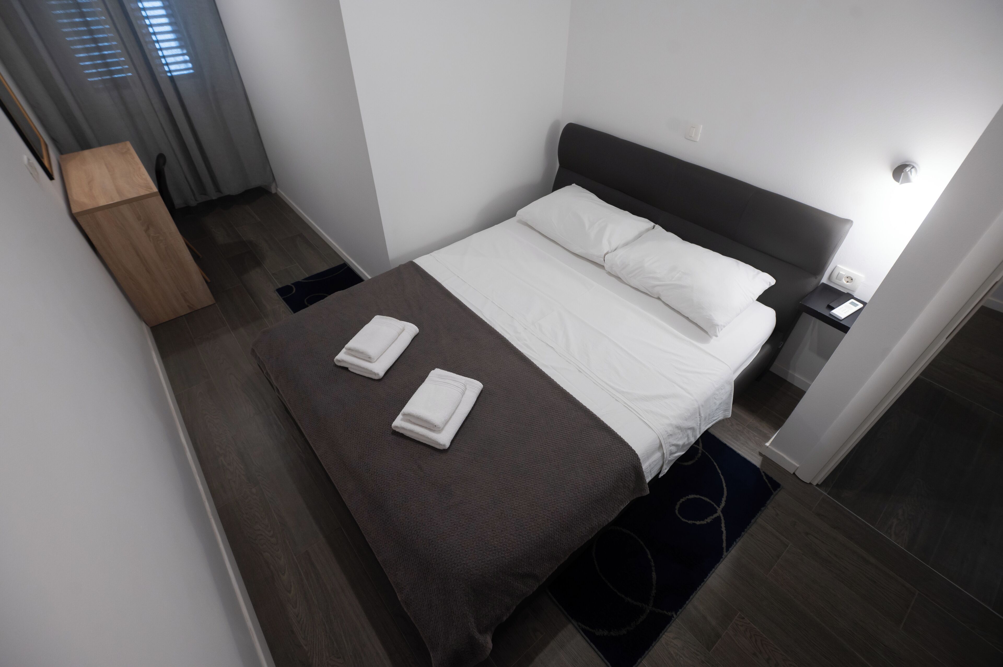 A neatly made bed with white and brown bedding, a bedside table with a lamp, and a small wooden cabinet.