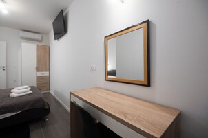Una habitación de hotel moderna con una cama, un escritorio de madera, un espejo y un televisor montado en la pared.