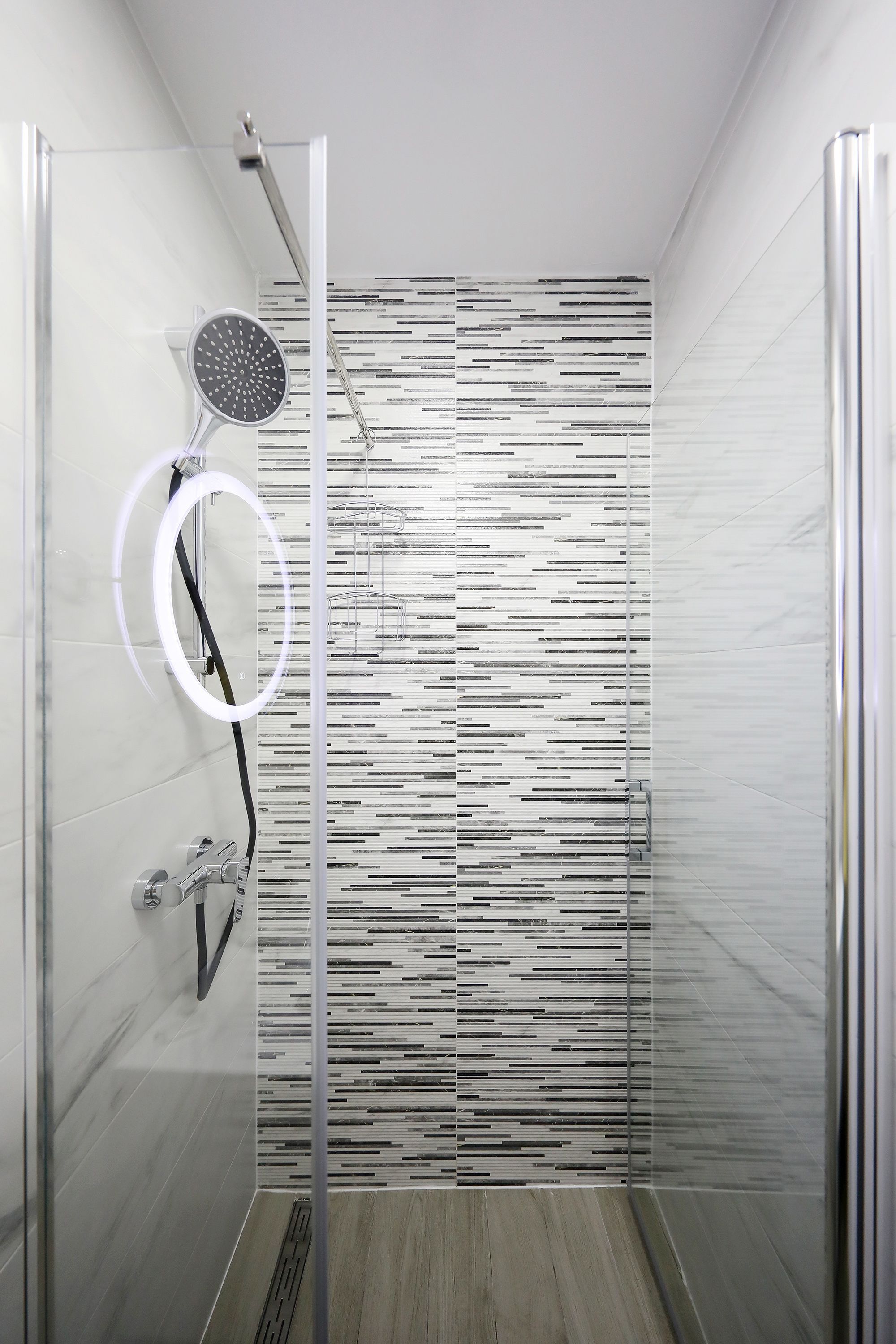 Ducha moderna con puerta de cristal, cabezal de ducha de mano y panel de control empotrado.