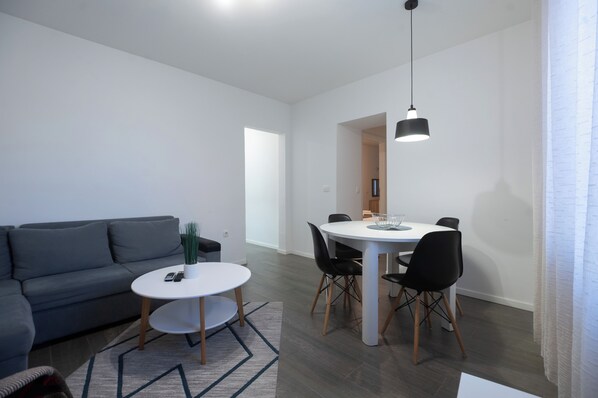 Una sala de estar moderna con un sofá gris, una mesa redonda de comedor con sillas negras y una lámpara colgante.