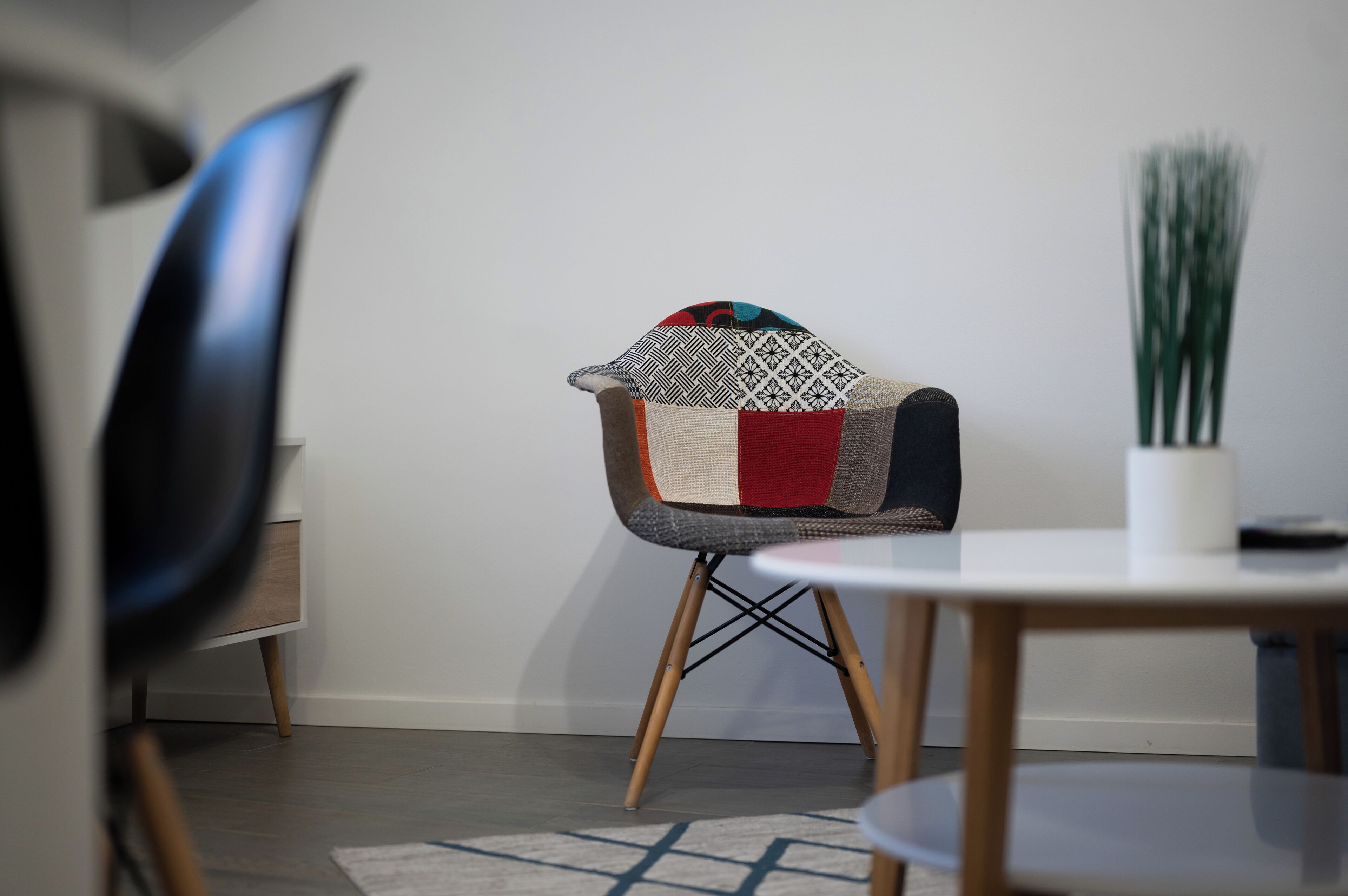 Een moderne eetruimte met een ronde tafel, een stoel met een kleurrijk patchwork kussen en een potplant.