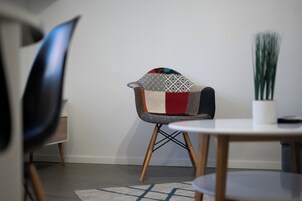 A modern dining area with a round table, a chair with a colorful patchwork cushion, and a potted plant.