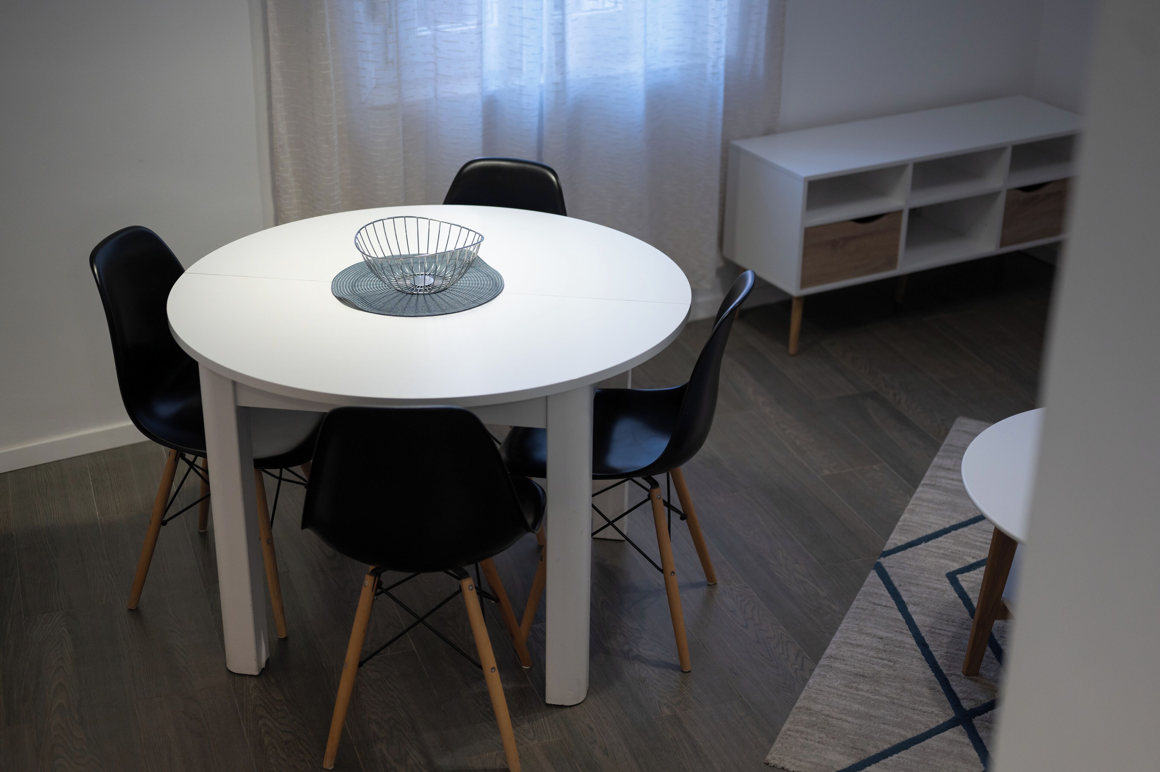 A dining area with a round white table, black chairs, and a white cabinet with drawers.
