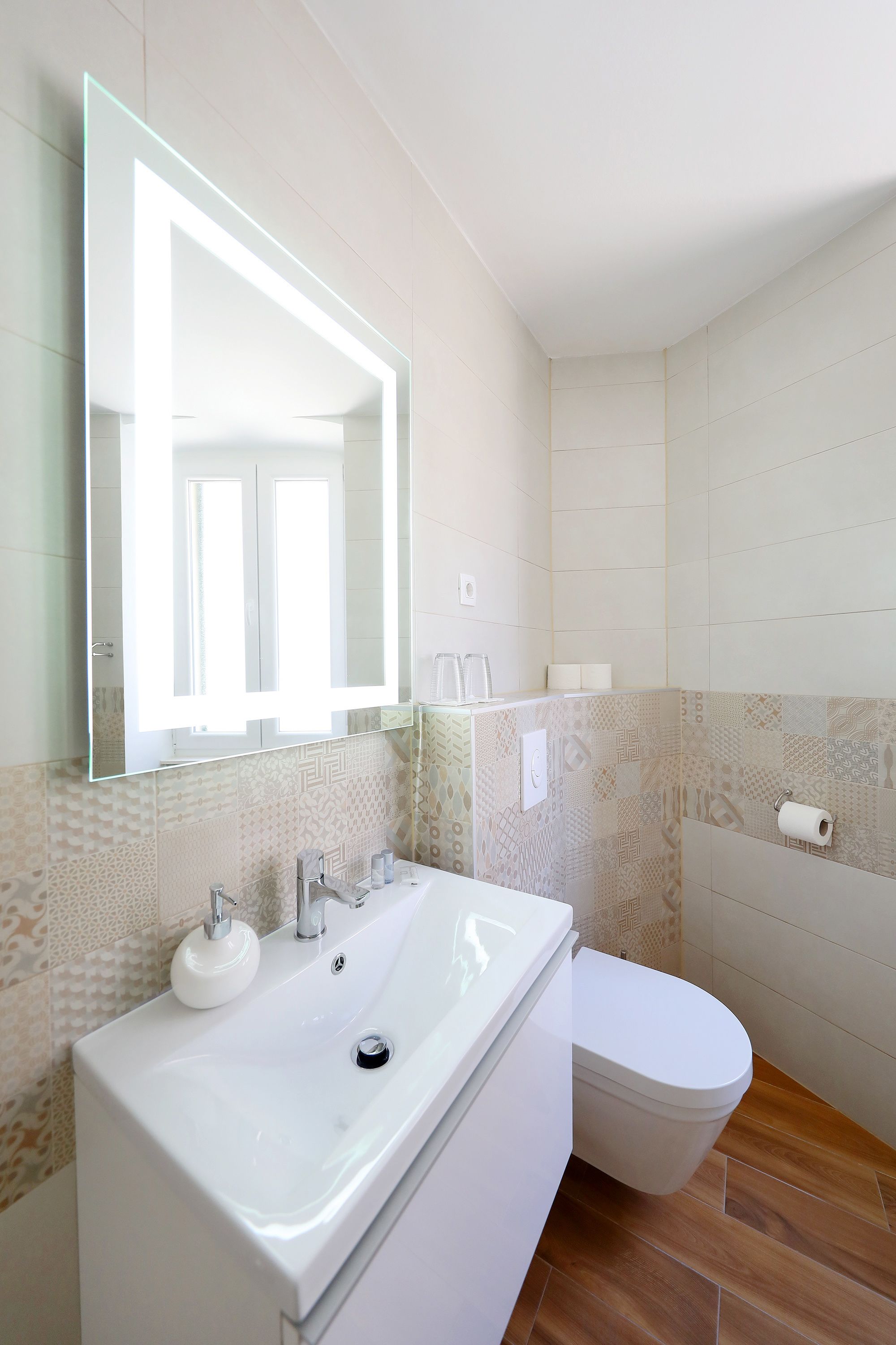 Een badkamer met een witte wastafel, een spiegel, een toilet en betegelde muren met een patroon.