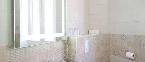 Een badkamer met een witte wastafel, een spiegel, een toilet en betegelde muren met een patroon.
