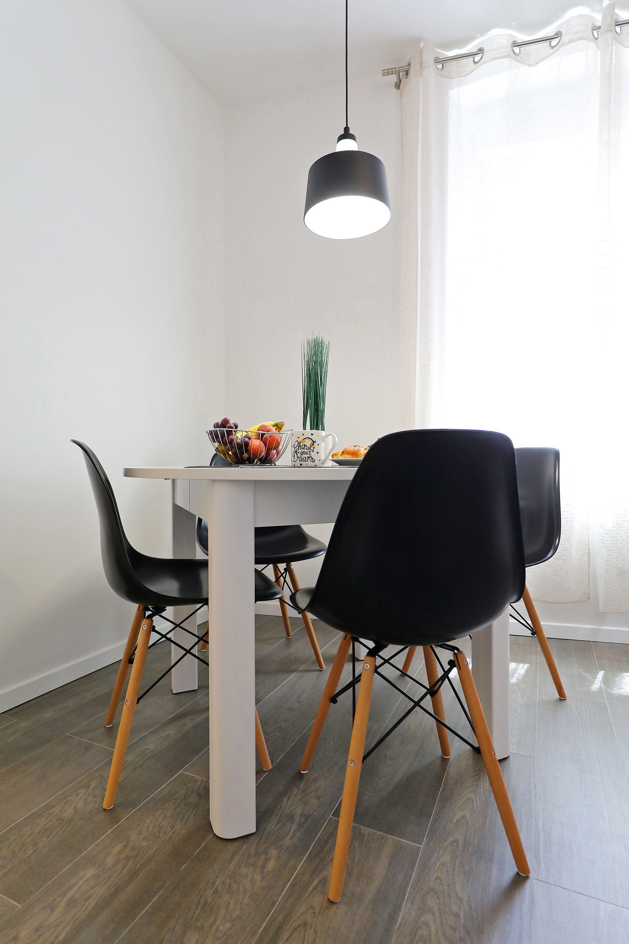 A dining area with a white table, black chairs, and a black pendant light.