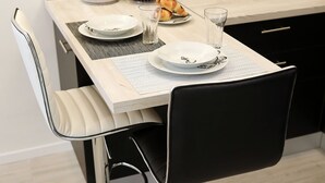 Un comedor moderno con una mesa de tonos claros dispuesta para dos personas, con un plato blanco, una copa y un cuenco de fruta.