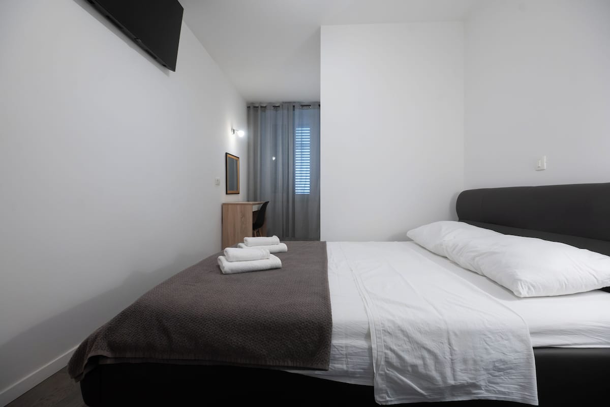 A modern hotel room with a large bed, a bedside table, a mirror, and a window with curtains.
