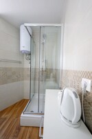 Un baño moderno con ducha de vidrio, un perchero y una tetera eléctrica blanca sobre la encimera.