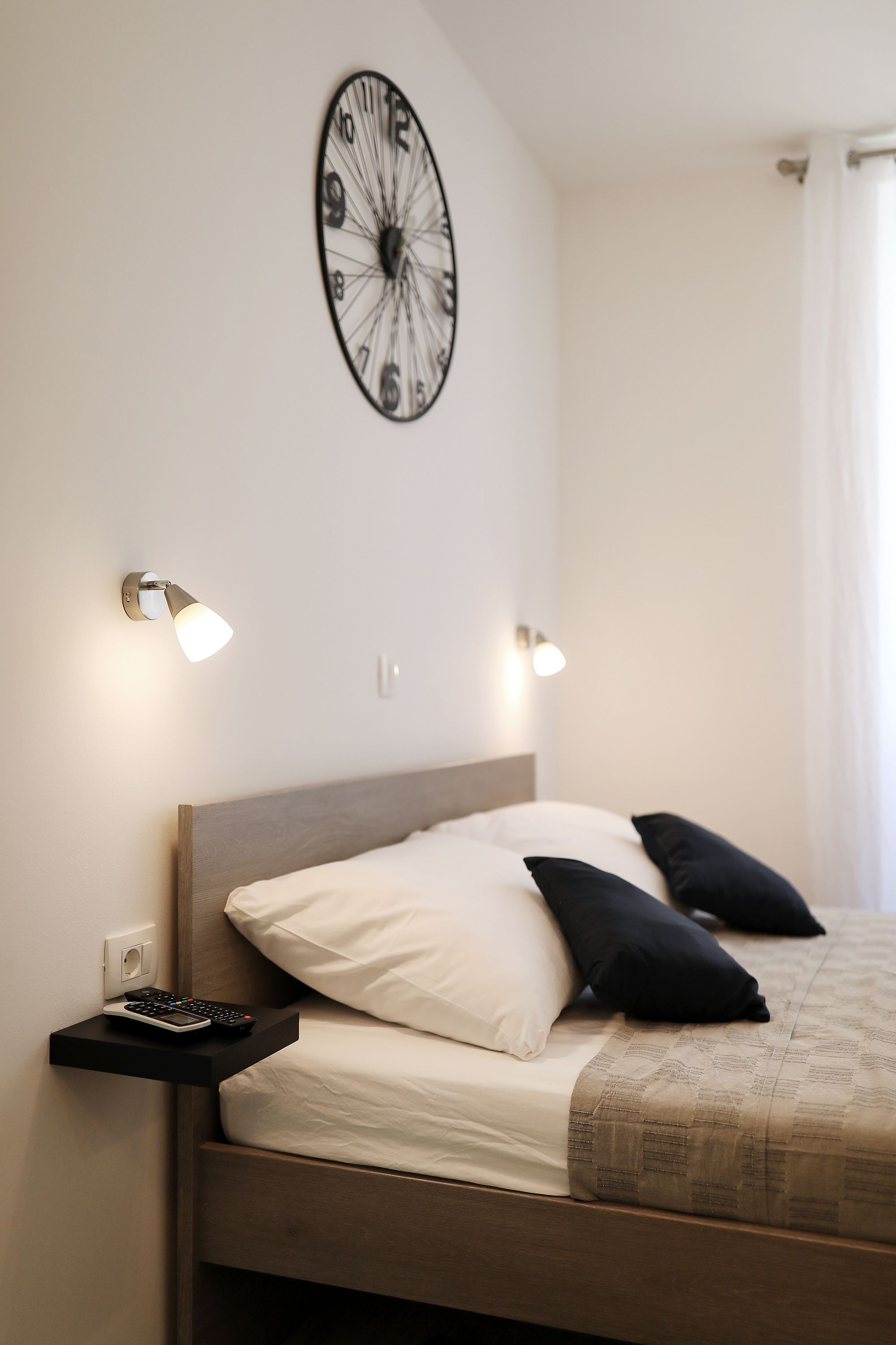 A neatly made bed with a wooden headboard, a wall clock, and bedside lamps.