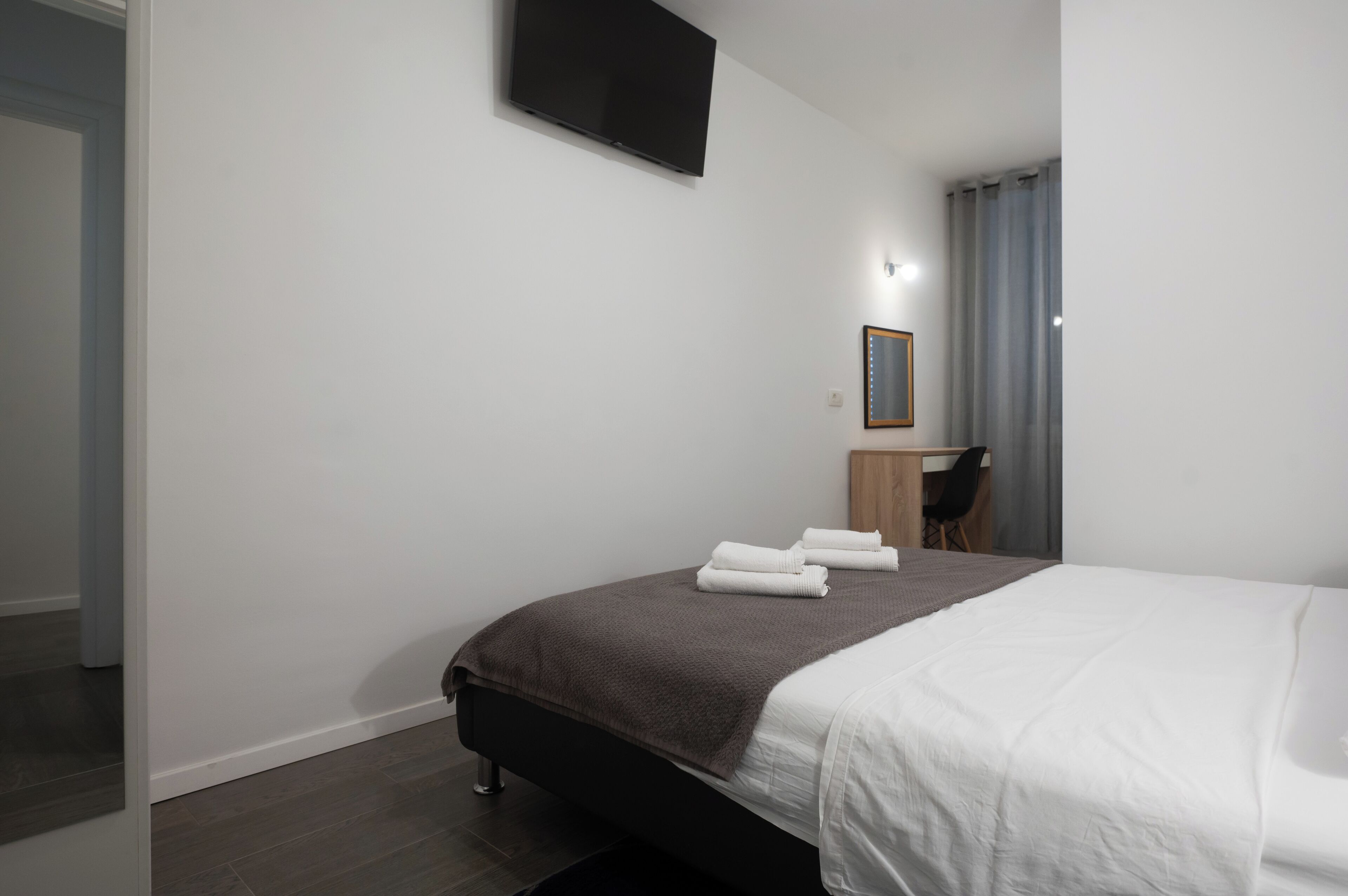 A modern hotel room with a bed, a desk, a chair, and a TV mounted on the wall.