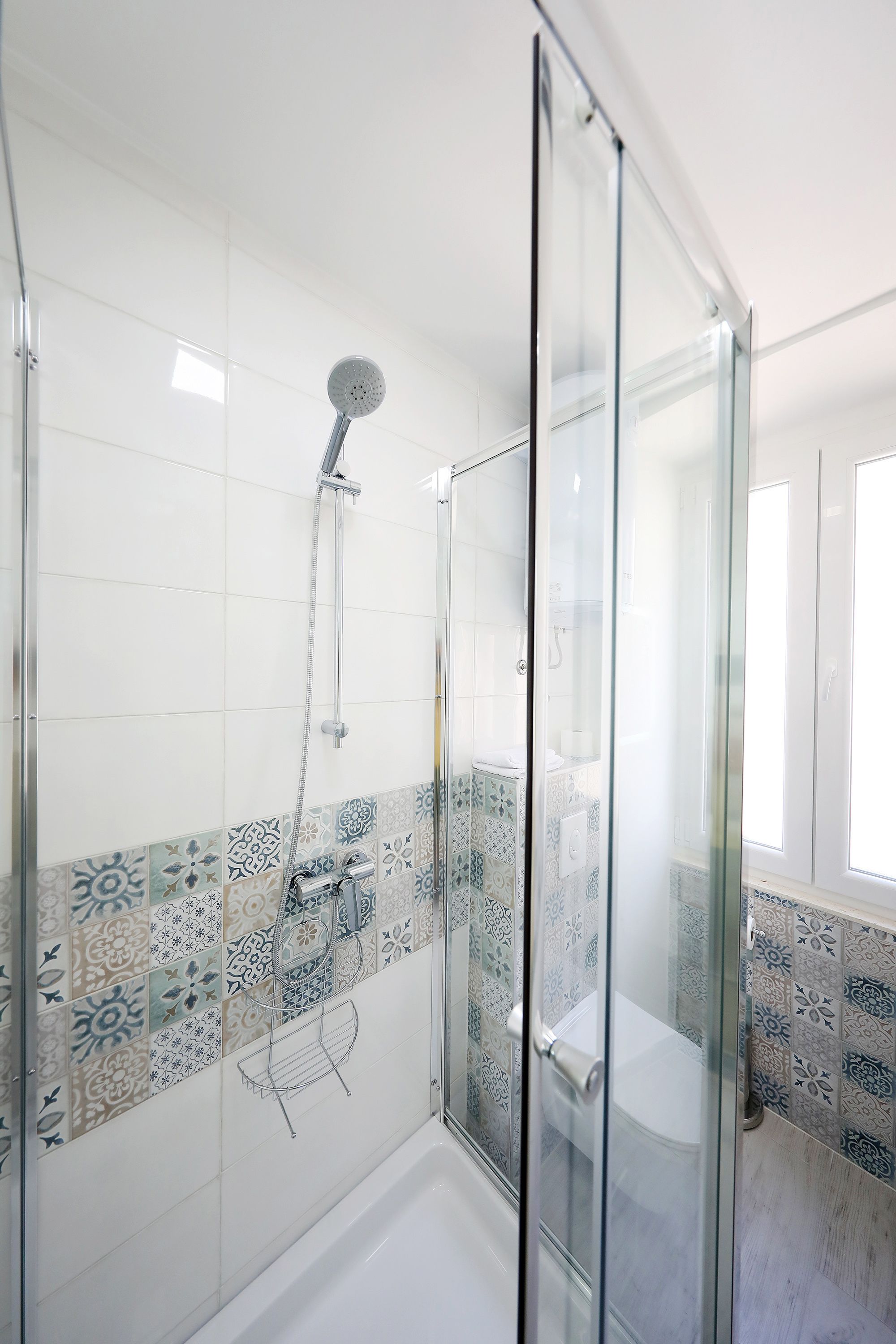 A modern bathroom with a glass shower enclosure, patterned tiles, and a white bathtub.
