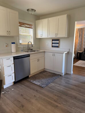 A modern kitchen with white cabinetry, a stainless steel dishwasher, and a window with blinds. - Charming & conveniently located 2BR Tacoma retreat close to everything you need (Tacoma)