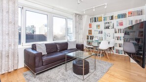 Ein modernes Wohnzimmer mit Ledersofa, Glastisch und einer Bücherwand voller Bücher.