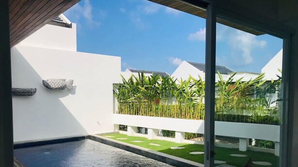 A modern outdoor pool area with a wooden deck, a hot tub, and a view of a lush garden with tall plants and a white fence. - Villa Ommy Hideway Residence No.108 (Ungasan)