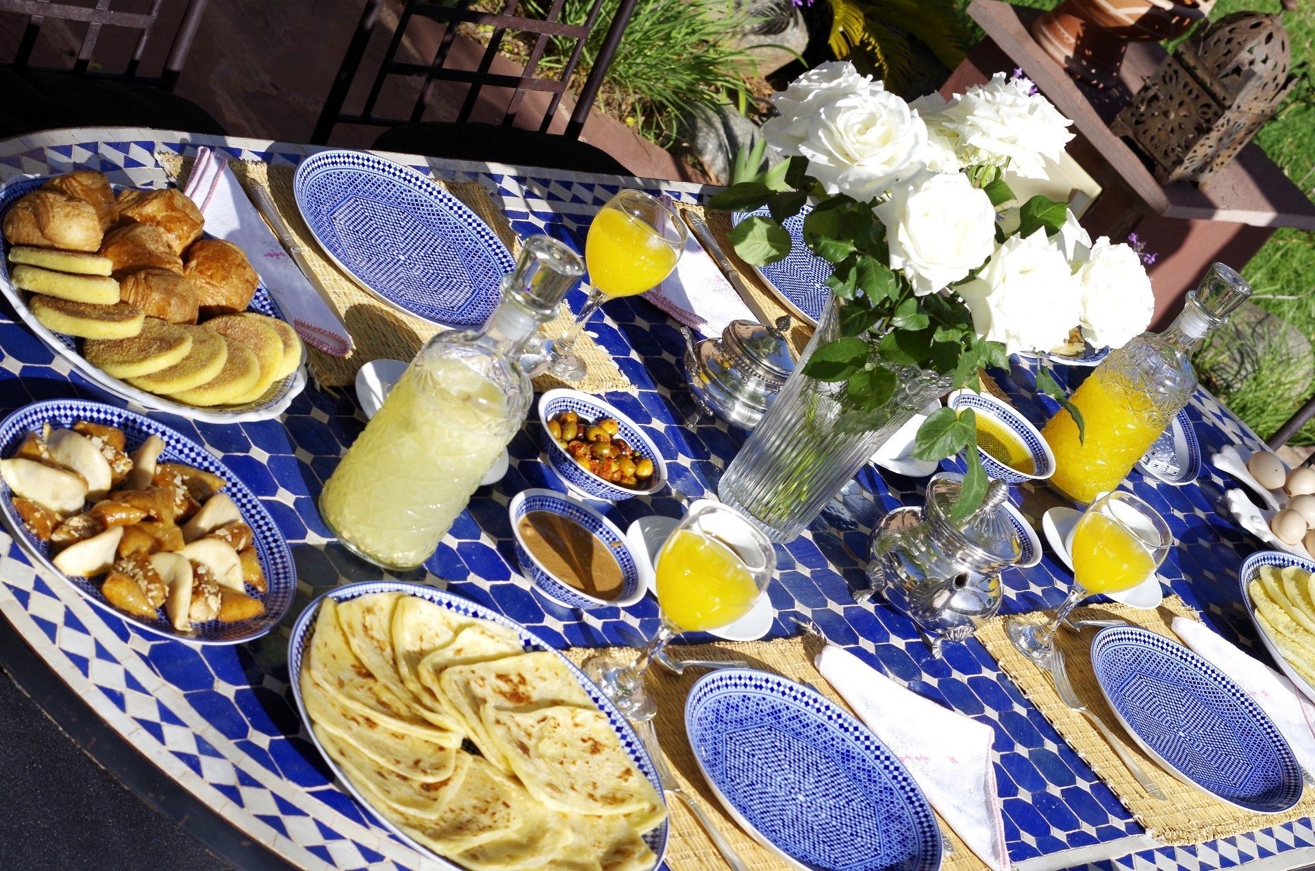 Una mesa dispuesta con diversos platos, incluyendo pasteles, panes planos y una botella de jugo de naranja, evocando un ambiente de desayuno o almuerzo ligero.