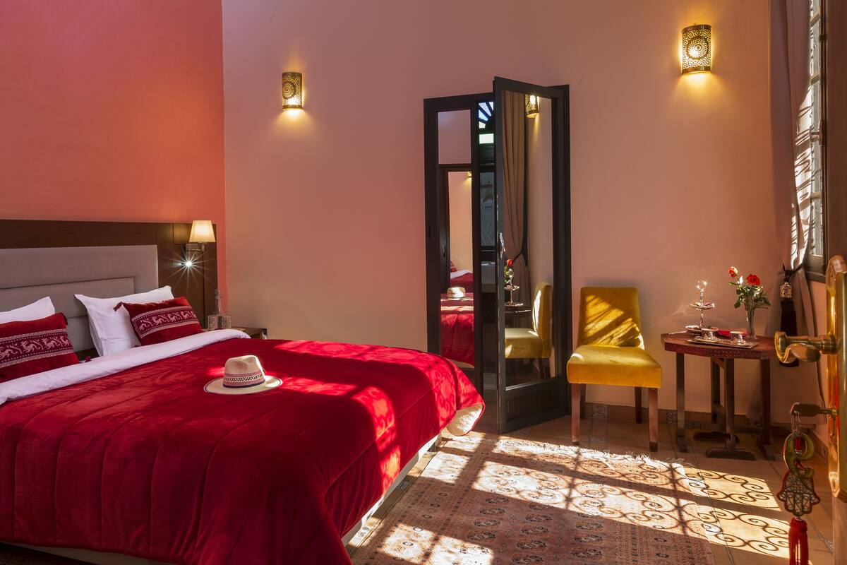 A hotel room with a large bed, a sitting area with a chair and table, and a mirror.