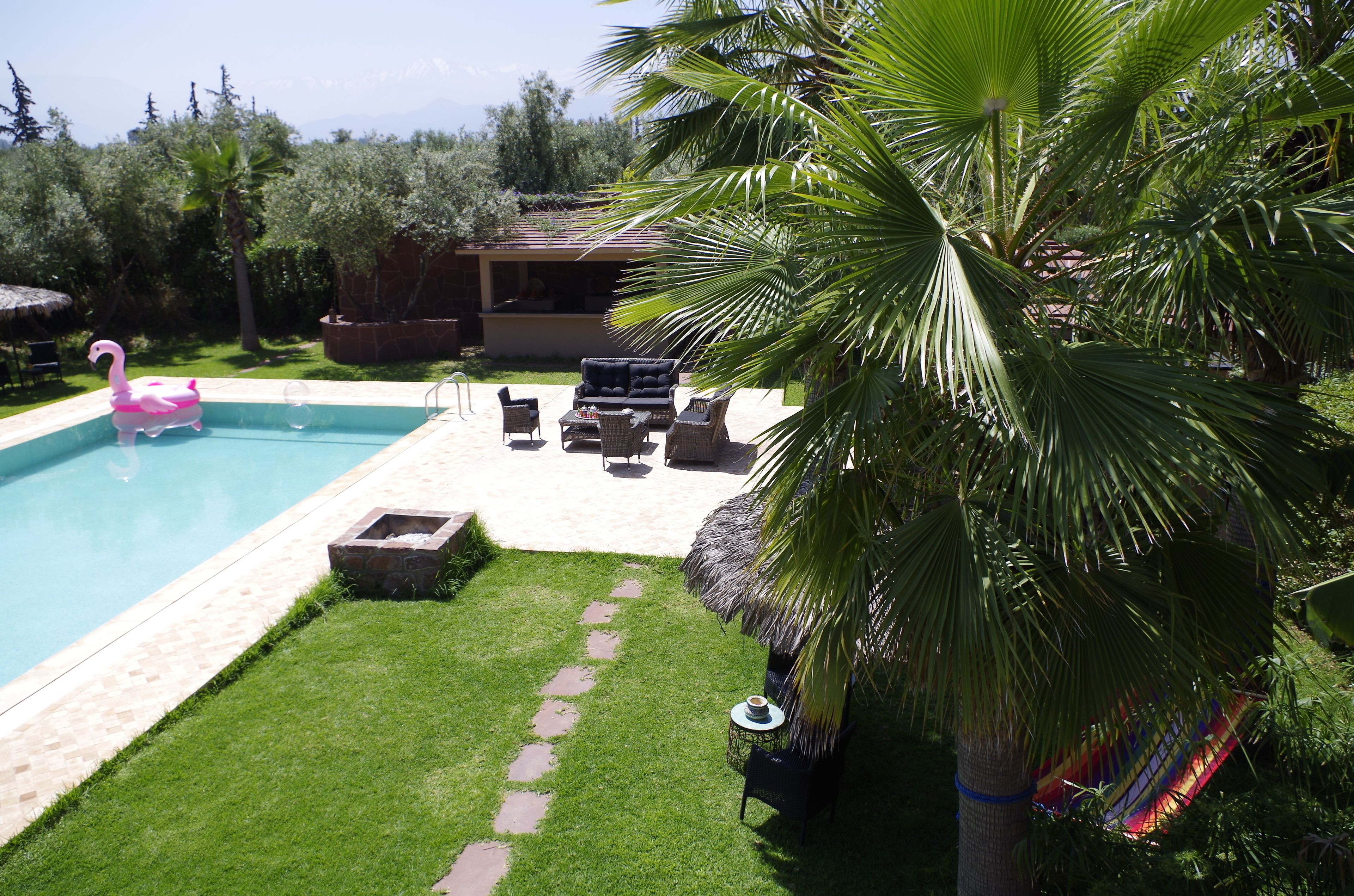A swimming pool with a flamingo float, a thatched-roof structure, and outdoor seating.