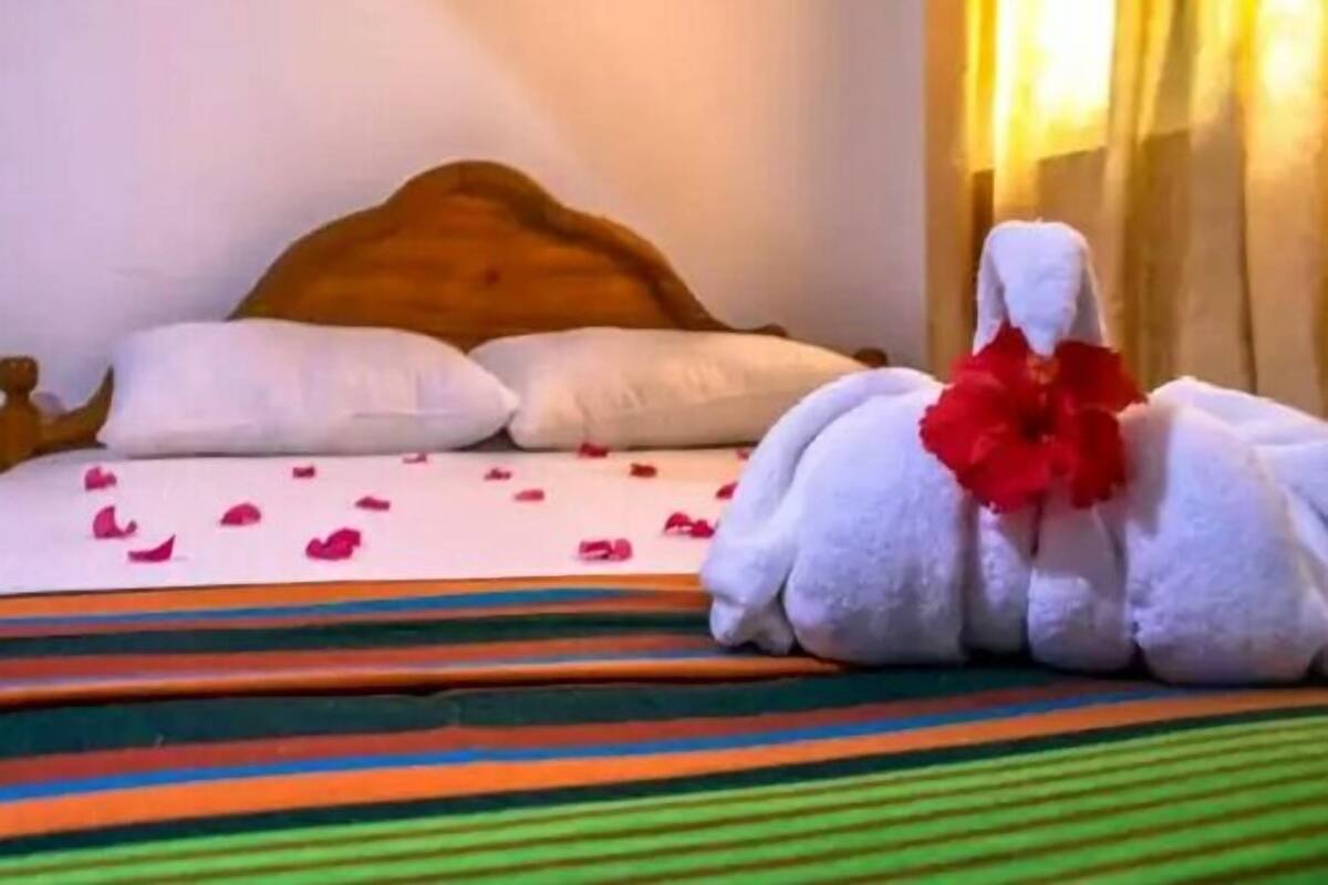 Una cama con almohadas blancas, una colcha a rayas y una toalla con una flor roja.