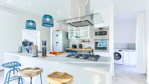 Een moderne keuken met een centraal eiland, roestvrijstalen apparatuur en blauwe hanglampen.