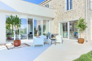 Une terrasse extérieure moderne, avec des meubles blancs, de grandes fenêtres et des plantes en pot.