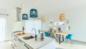Een moderne keuken met een centraal eiland, een eethoek met blauwe stoelen en hanglampen.