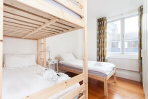 A dormitory room with bunk beds, a small bedside table with a lamp, and a window with curtains. - Spacious Apartment Berwick St &Oxford St (London)