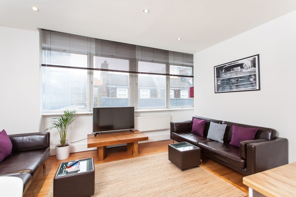 A modern living room with a leather sofa, a wooden coffee table, and a flat-screen TV. - Spacious Apartment Berwick St &Oxford St (London)