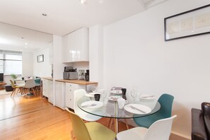 A modern kitchen with white cabinets, a dining area with a glass table, and a framed picture on the wall. - Spacious Apartment Berwick St &Oxford St (London)