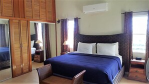 Un dormitorio con una cama grande, un armario de madera, una mesita de noche con lámpara y una ventana con cortinas.