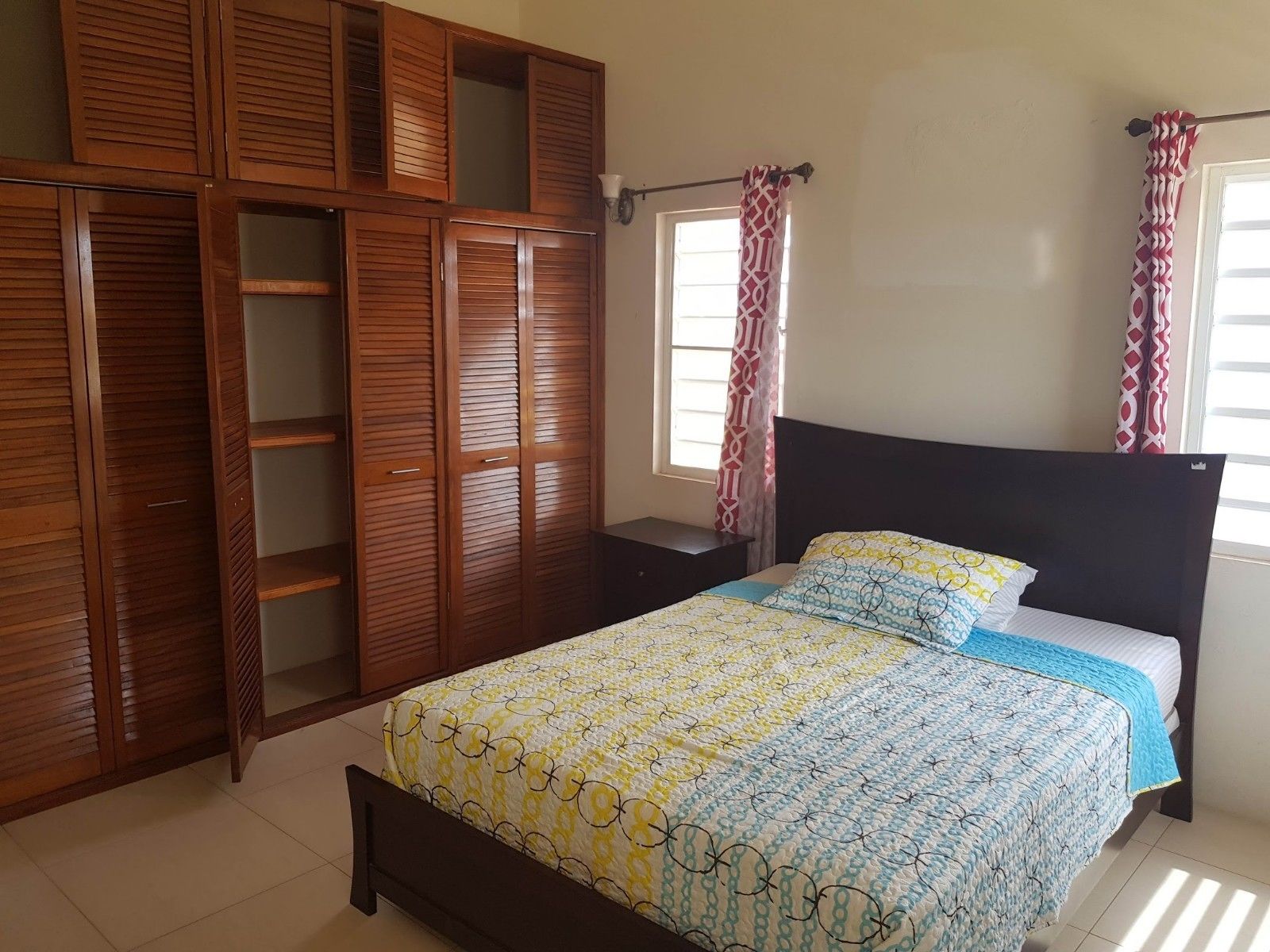 A bedroom with a bed, wooden wardrobe, and a window with curtains.