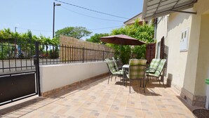 Un patio al aire libre con suelo de baldosas, una mesa con sillas y un paraguas grande.