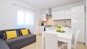 A modern apartment with a grey sofa, white dining table, and a kitchen area. - Apartment Maja (Vrsi)