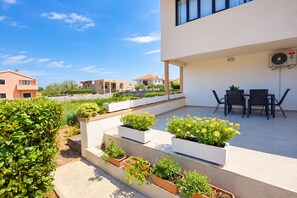A modern outdoor patio with a dining area, planters with flowers, and a view of neighboring houses. - Apartment Maja (Vrsi)