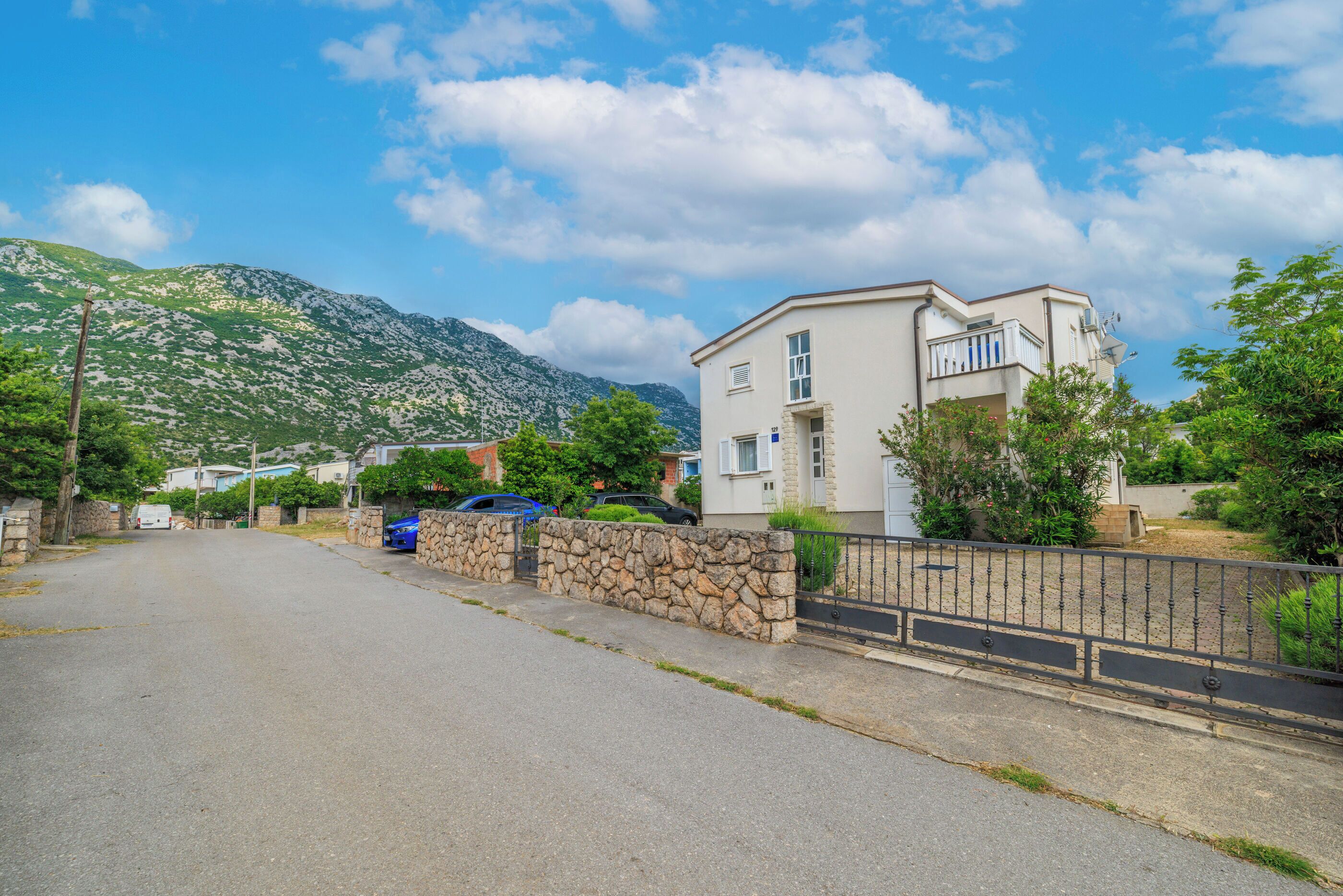 Una calle residencial con una casa de dos pisos, un muro de piedra y una montaña al fondo.