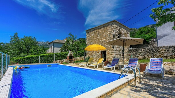 A swimming pool with lounge chairs and umbrellas, surrounded by stone walls and greenery. - House Katica (Grizane)
