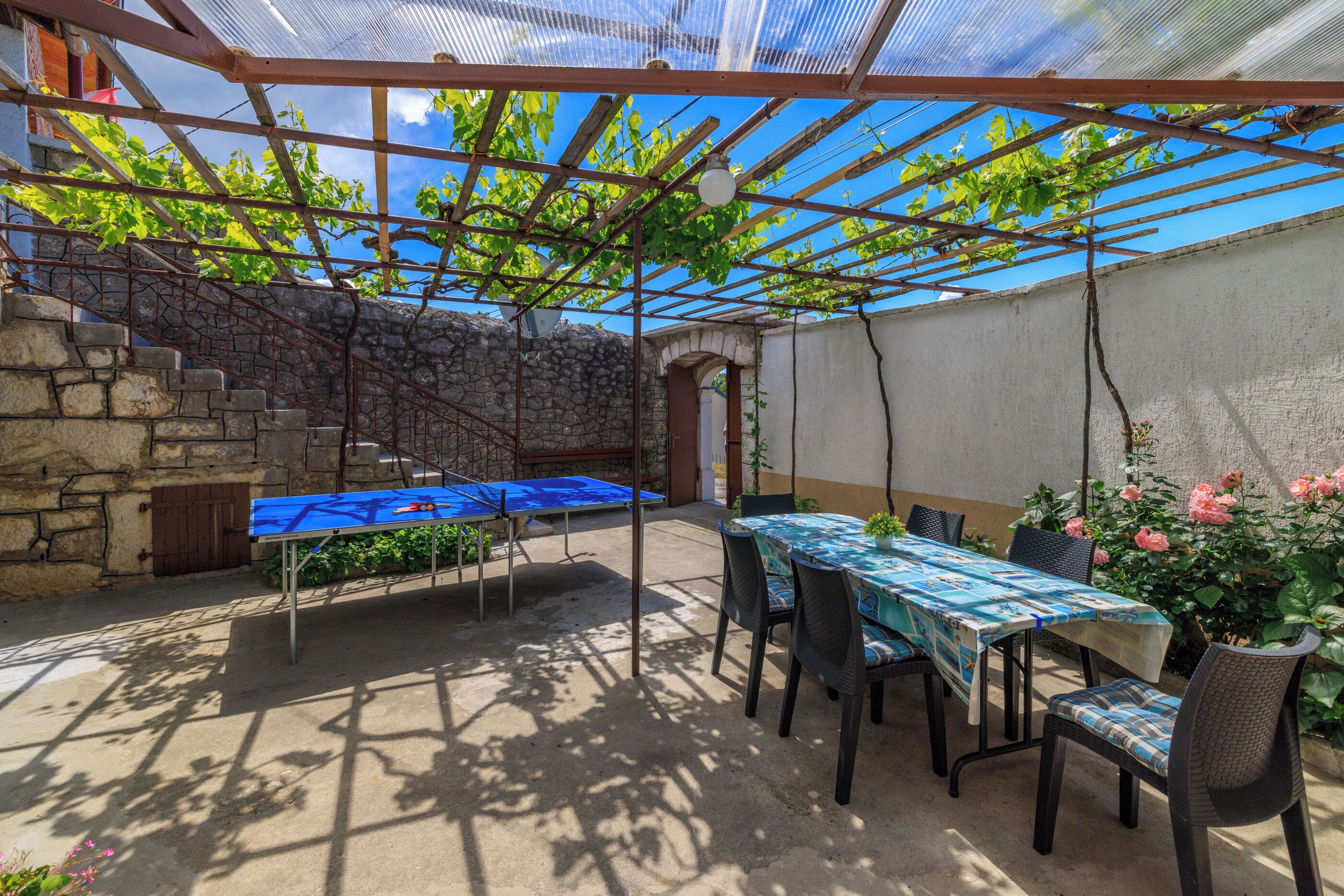 Un patio exterior con una pérgola, escalones de piedra y una mesa con sillas.
