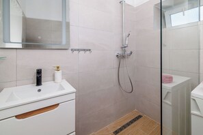 A modern bathroom with a glass shower enclosure, a white sink with a faucet, and a mirror above the sink.