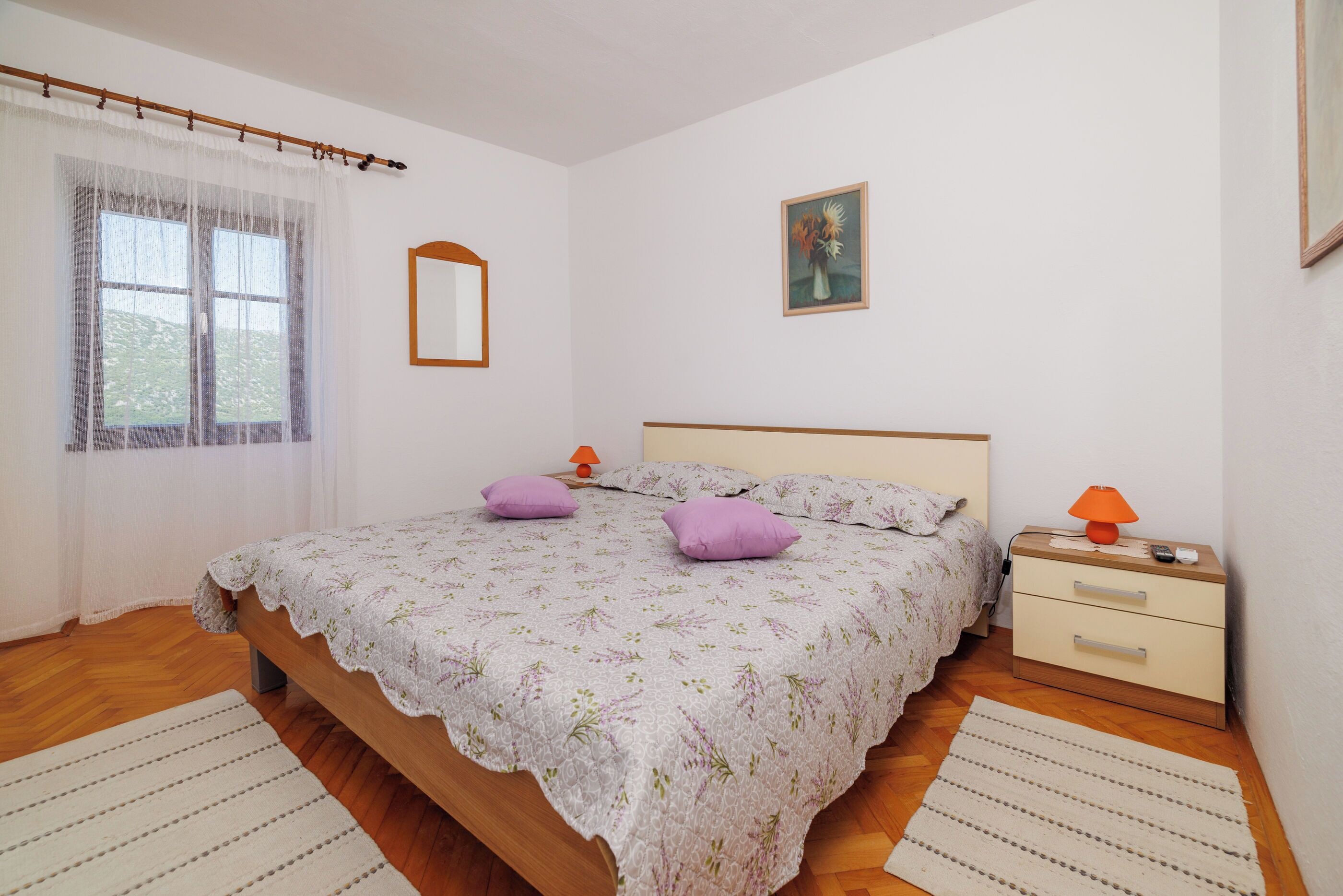 Un dormitorio con cama, mesita de noche, lámpara, espejo y ventana con cortinas.