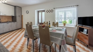 A dining area with a table set for four, chairs, a television, and a window with curtains. - House Katica (Grizane)