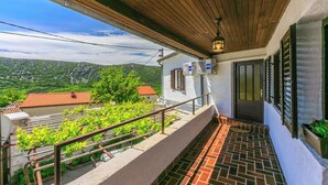 A balcony with a tiled floor, a wooden ceiling, and a view of a green landscape. - House Katica (Grizane)
