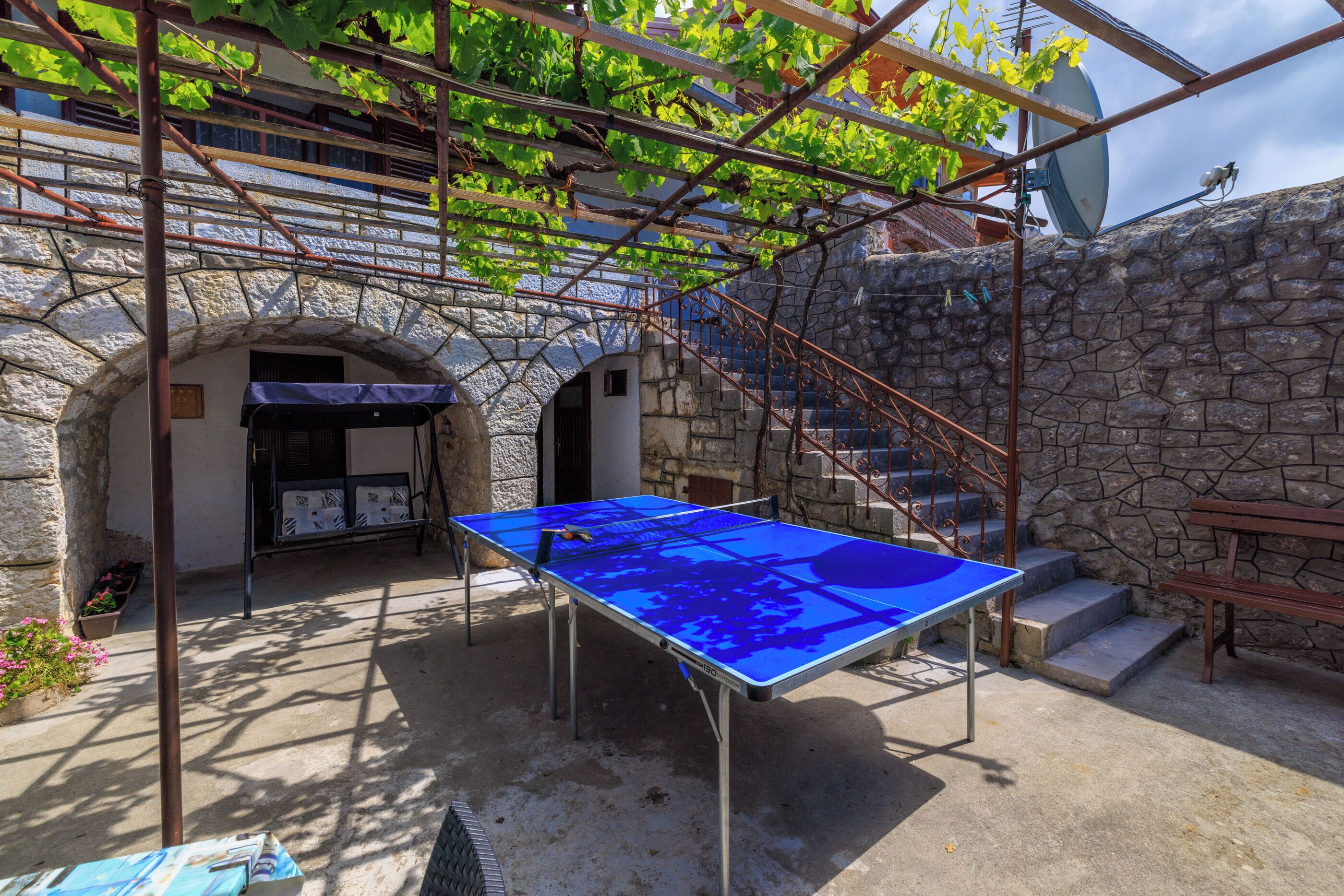 A courtyard with a ping pong table, stone walls, and a metal pergola.