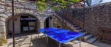 A courtyard with a ping pong table, stone walls, and a metal pergola.