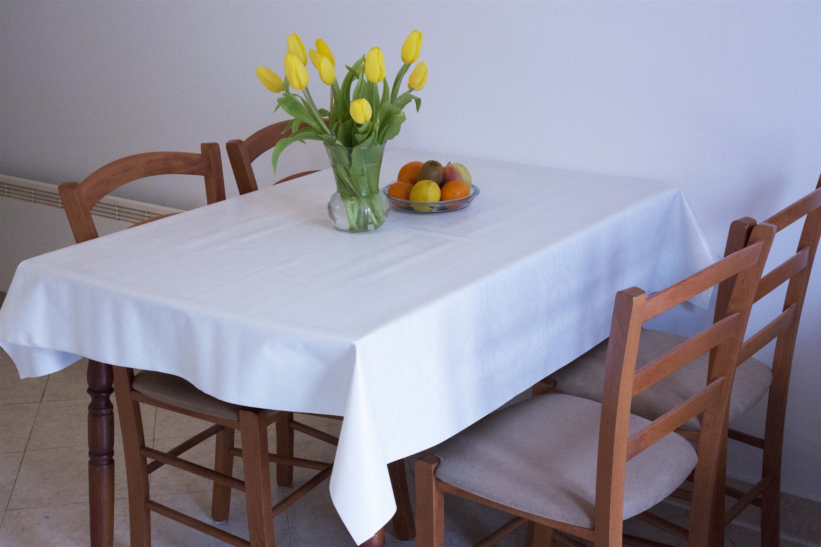 Une table à manger recouverte d’une nappe blanche, entourée de chaises en bois dotées d’assises rembourrées.