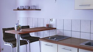 A kitchen with a wooden table, wicker chairs, a stainless steel sink, and white cabinets.