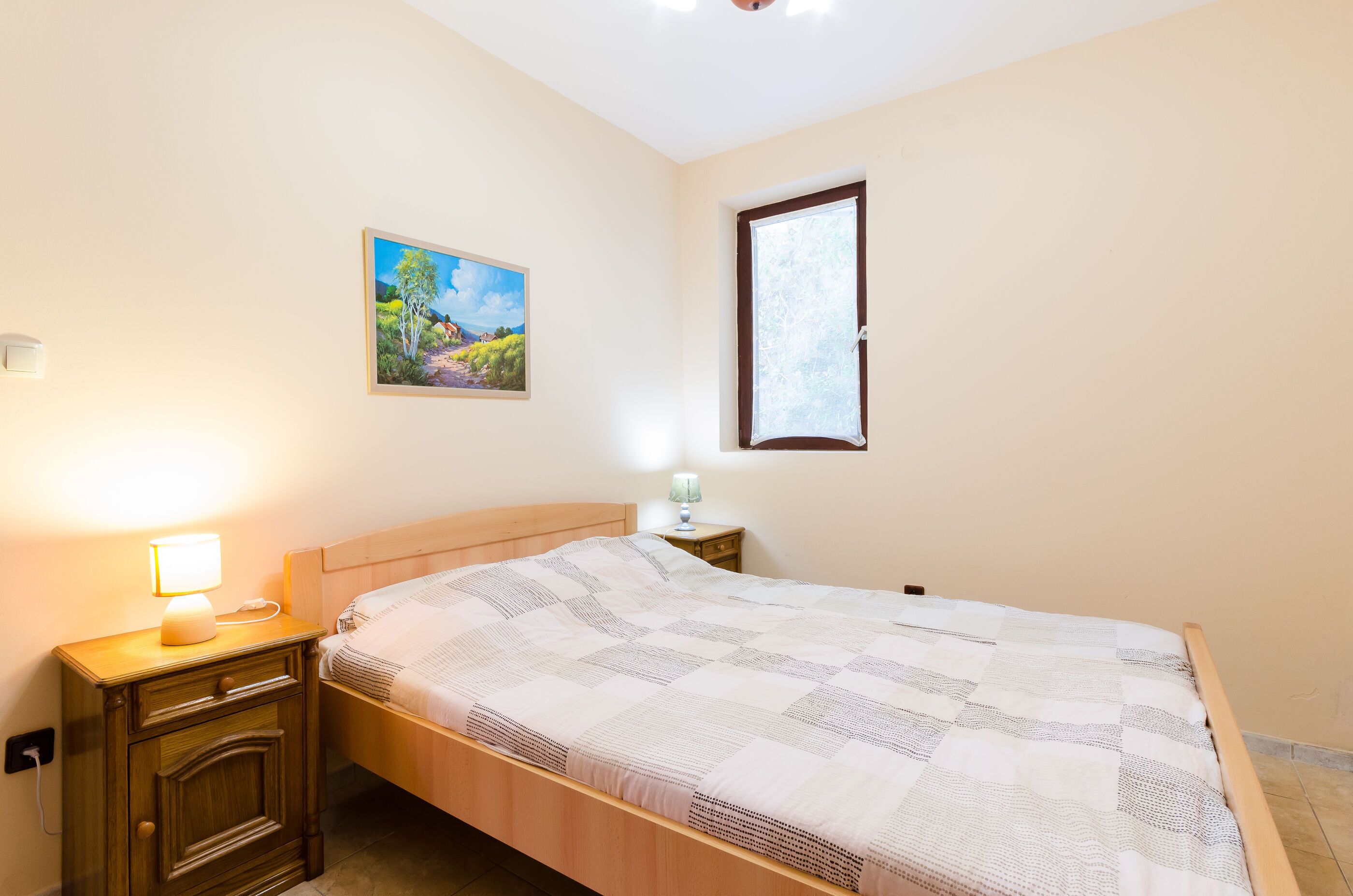 Un dormitorio con cama, mesita de noche, lámpara y un cuadro en la pared.