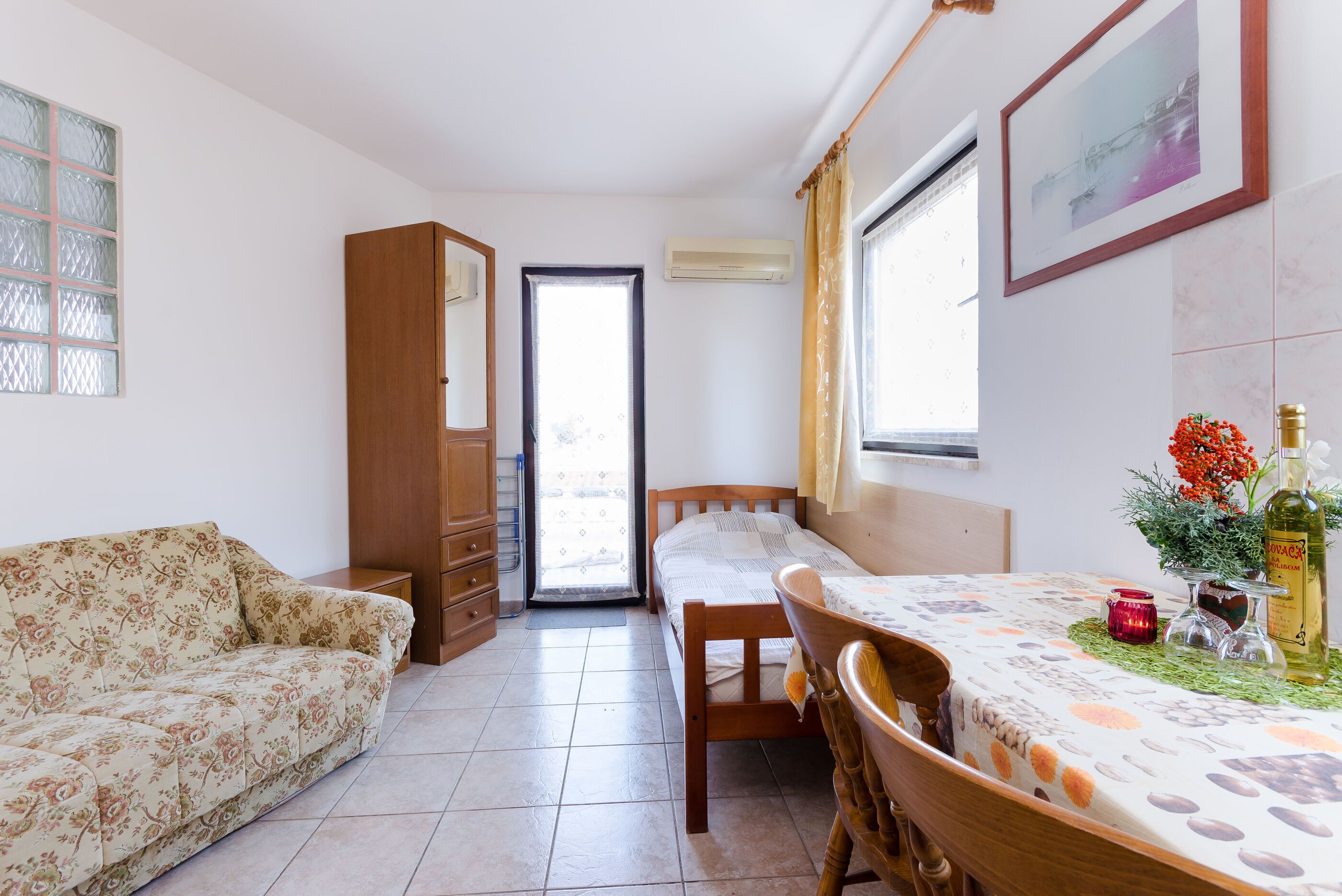 A room with a bed, a sofa, a dining table, and a window.
